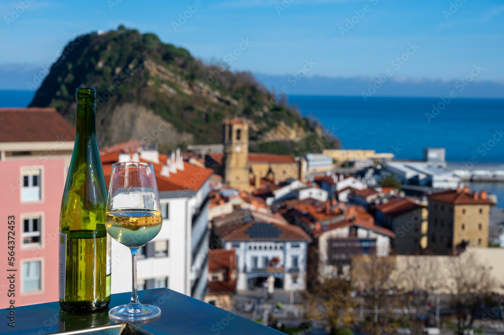 Tasting of txakoli or chacolí slightly sparkling very dry white wine produced in Spanish Basque Country with view on old port and village Getaria, Spain