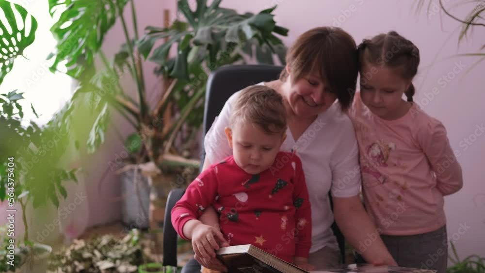 Grandmother shows her grandchildren an album of photographs. Children and grandmother look at the photo album. Grandmother shows her grandchildren an album of photographs. Children and grandmother look at the photo album.