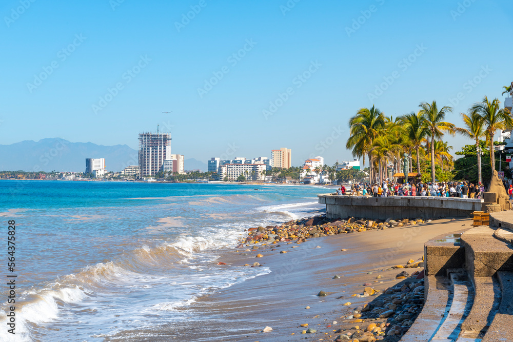 The sandy beach alongside the Malecon promenade boardwalk and Zona Romantica area of Puerto Vallarta, Mexico, with the sea and city skyline in view.