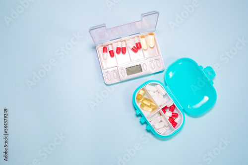 Plastic box with different pills on light blue background, top view. 
