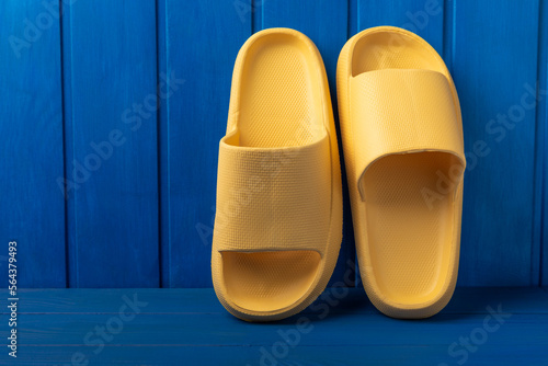Yellow rubber summer slippers. Replacement shoes for home or office. Yellow slippers on a background of blue space. Relax concepts. Space for text.Space for copy.
