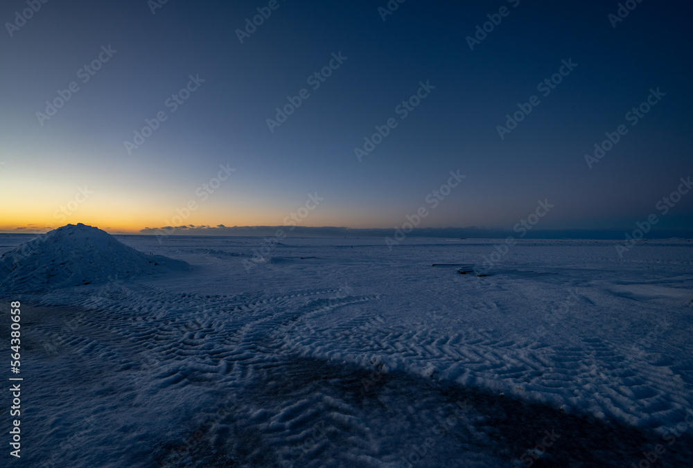 Road and flat snowy landscape in almost darkness with tire tracks going to the horizon with the sun rising in a magical golden Icelandic sunrise. Road and flat snowy landscape in almost darkness with tire tracks going to the horizon with the sun rising in a magical golden Icelandic sunrise.
