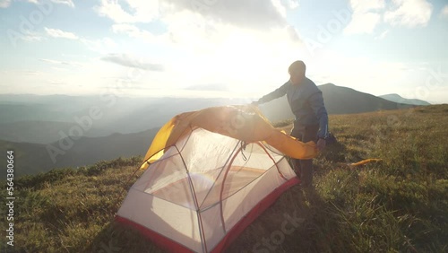 A man sets up a tent in the mountains at sunset. Camping by a tourist during a hike. A boy prepares to sleep on top of a mountain. Rest and freedom. High quality 4k footage