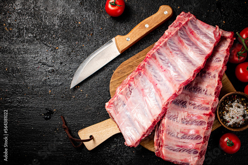 Raw ribs on a wooden cutting board with spices and tomatoes. 