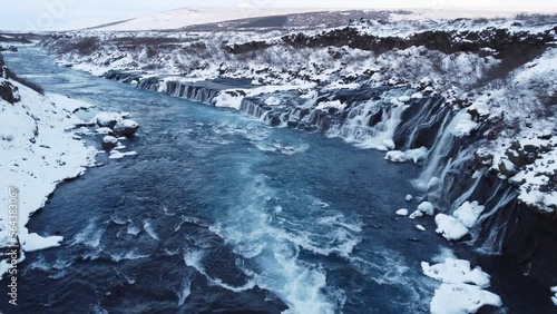 Waterfall in Iceland, Snowy Mountain with Cold River in Winter, Magical Winter Time Location, Blue Glacial Water with a Huge Current. Pure Scenic Landscape. Hraunfossar. 