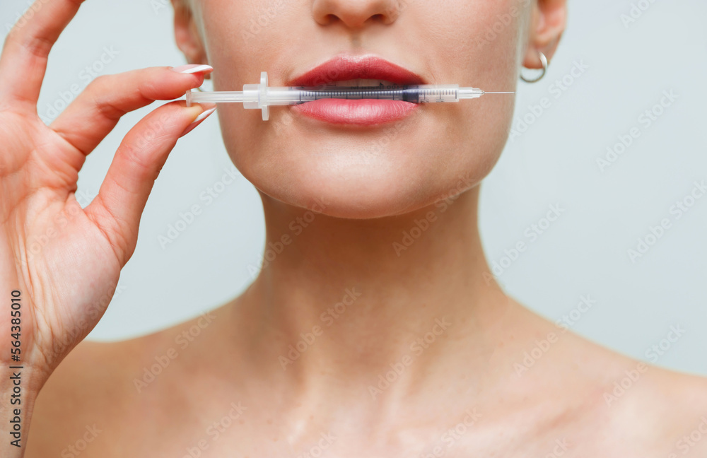 Closeup face young woman holds syringe in mouth. Hyaluronic acid collagen injection for lips Closeup face young woman holds syringe in mouth. Hyaluronic acid collagen injection for lips
