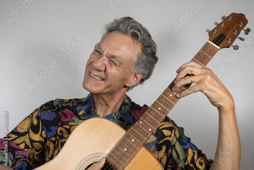 Senior man wearing a colorful shirt playing his acoustic guitar 