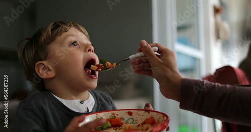 Kid open mouth eating food mother feeds child with spoon