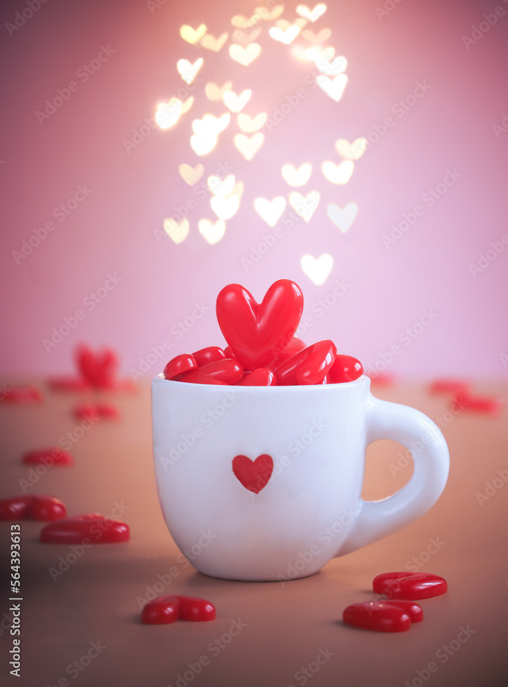 A white mug containing red mini hearts inside of it, with light illumination of heart bokeh with pink background. Valentine's day concept A white mug containing red mini hearts inside of it, with light illumination of heart bokeh with pink background. Valentine's day concept