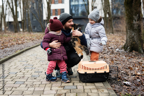 Father and daughters with cat in travel pet plastic cage carriage outdoor at park. © AS Photo Family