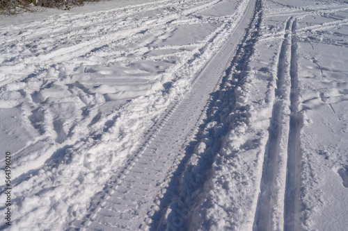 Tracks of a snowmobile next to cross country skiing and foot steps in white snow