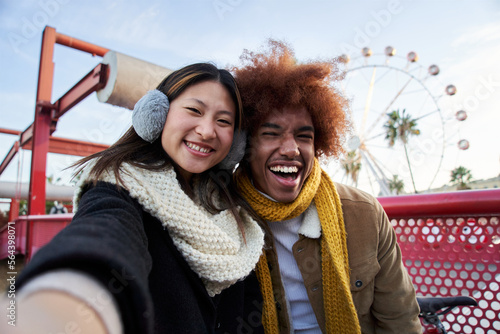 Young mixed race couple in winter clothes taking a selfie outdoors. Excited students smiling and looking at the camera. Couple concept, nice, happy, friendship, millennial hipster.