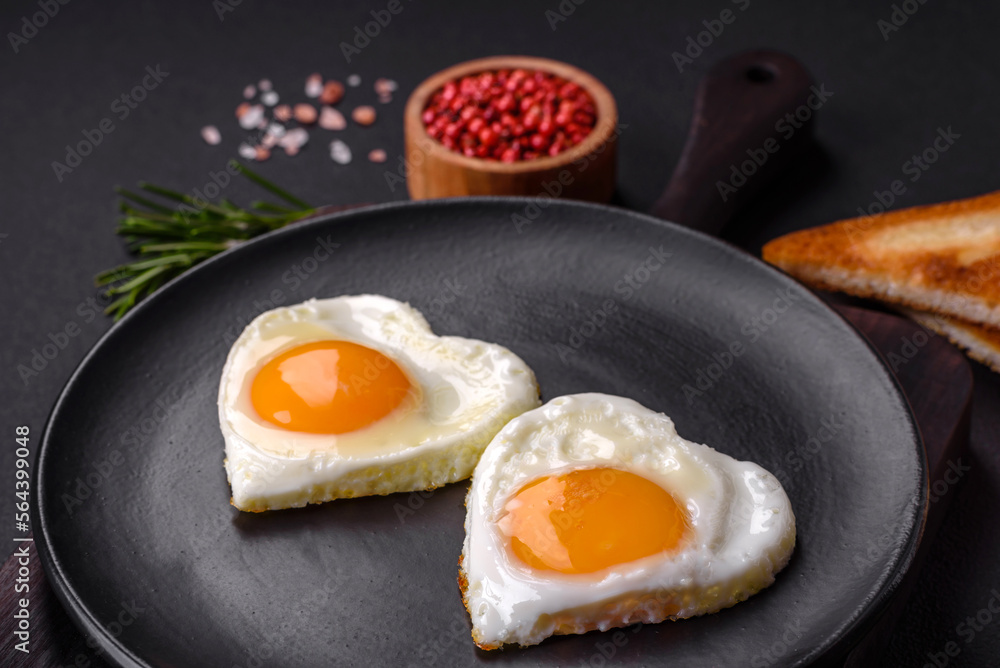Two heart-shaped fried eggs on a black ceramic plate on a dark concrete background Two heart-shaped fried eggs on a black ceramic plate on a dark concrete background