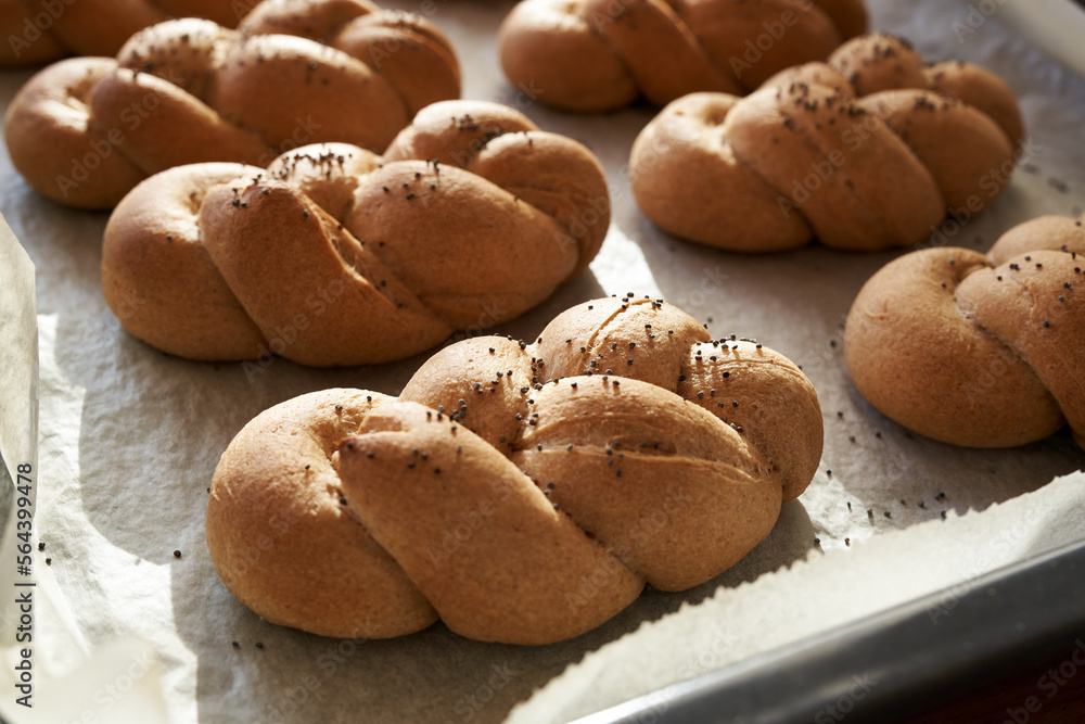 Homemade braided bread rolls made of whole grain spelt flour on a baking sheet in sunlight