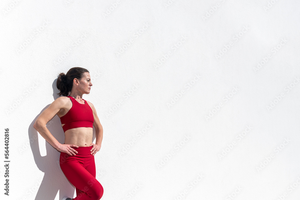 Sporty woman with hands on her hips leaning against a white wall in the sun. Sporty woman with hands on her hips leaning against a white wall in the sun.