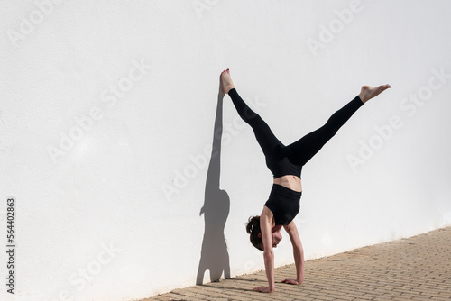 Obraz na plátně Woman doing a handstand against a white wall in the sun