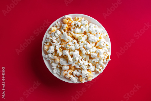 Tasty cheese popcorn in bowl isolated on red background. Top view, flat lay. Fast food, movies, cinema and entertainment concept.