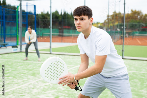 Portrait of young sporty guy playing paddle tennis with friends on open court. Active lifestyle concept © JackF