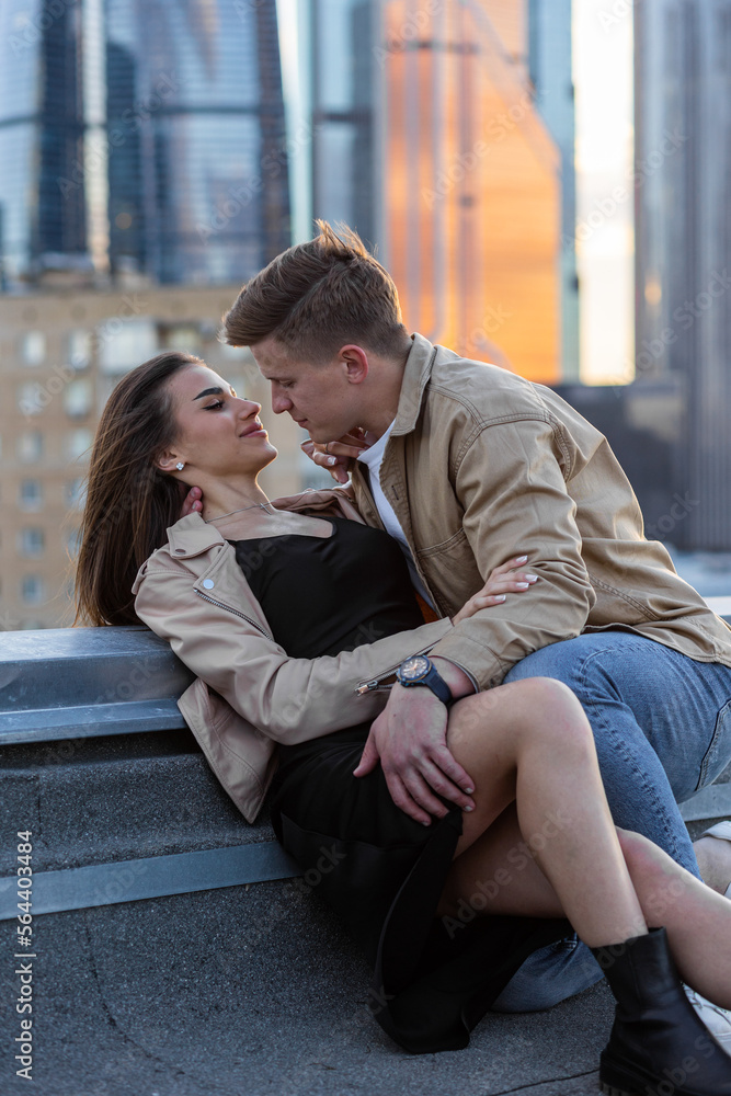 Young happy beautiful loving couple on a surprise romantic date on a rooftop on a Saint Valentine's Day. Attractive man and woman, male and female hugging, kissing. Sunset, skyscrapers urban view Young happy beautiful loving couple on a surprise romantic date on a rooftop on a Saint Valentine's Day. Attractive man and woman, male and female hugging, kissing. Sunset, skyscrapers urban view
