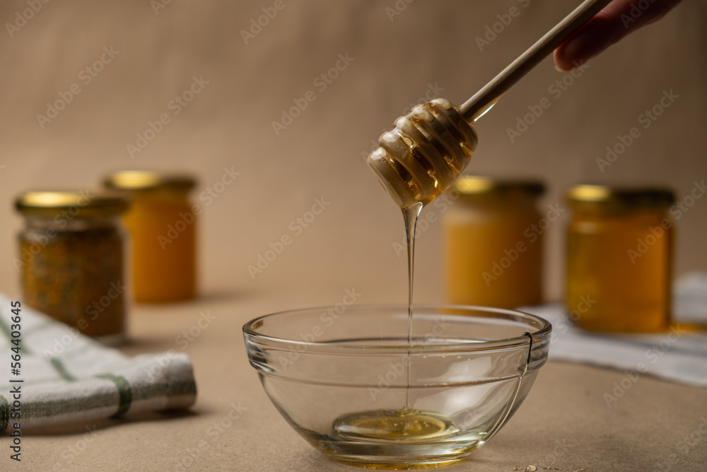 A bowl of honey. A beautiful female hand takes a honey dipper on a background of kraft paper. A bowl of honey. A beautiful female hand takes a honey dipper on a background of kraft paper.
