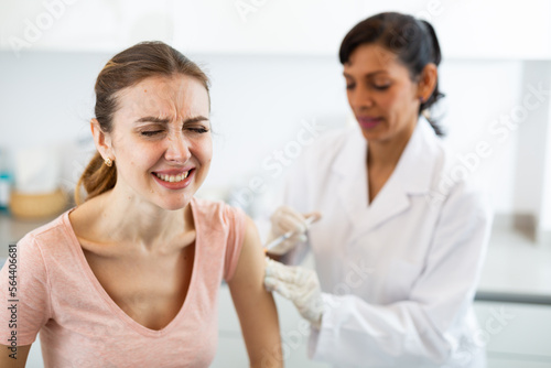Portrait of scared young adult woman getting injection during visit at doctors office