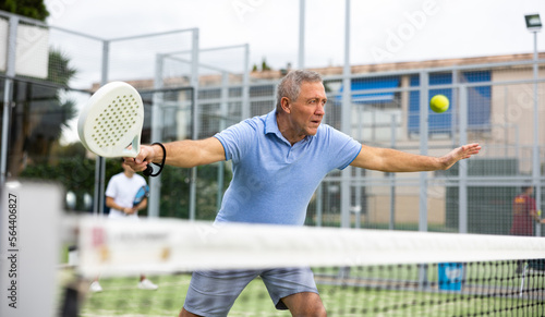 Emotional mature male playing padel behind the net during match on tennis court in autumn © JackF