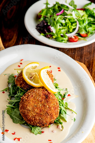 Crab cake. Crab cake served with spicy rémoulade sauce on top of a mixed green salad. Jumbo crab meat mixed with garlic, onions, spices and fried in butter. Classic American restaurant appetizer.