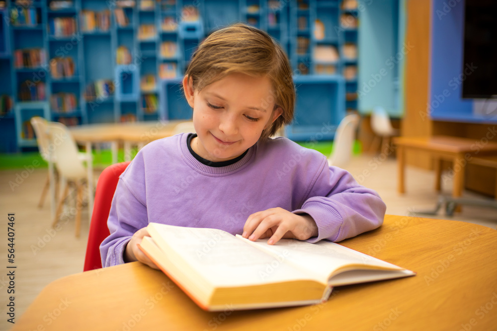 boy reading a book, doing homework while sitting at a table in a classroom or library boy reading a book, doing homework while sitting at a table in a classroom or library