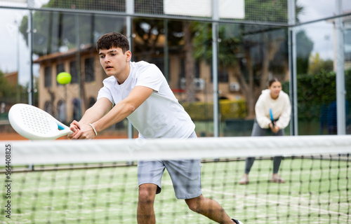Portrait of sporty young guy hitting two handed backhand during paddle tennis friendly match in open court on warm autumn day © JackF