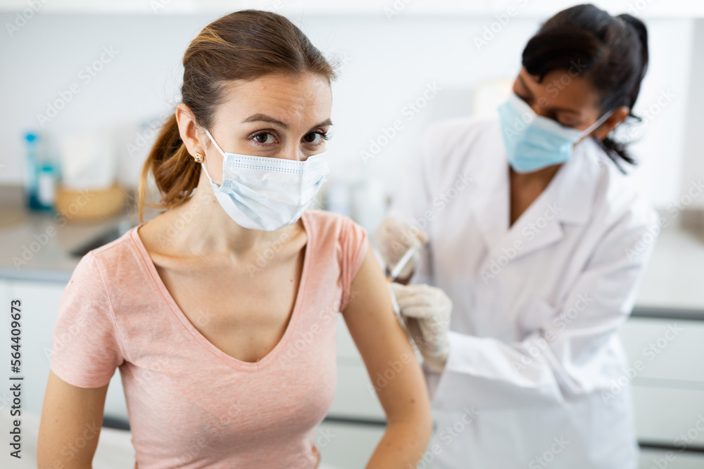 Young adult woman in medical face mask getting vaccinated at doctors office, coronavirus or flu vaccination