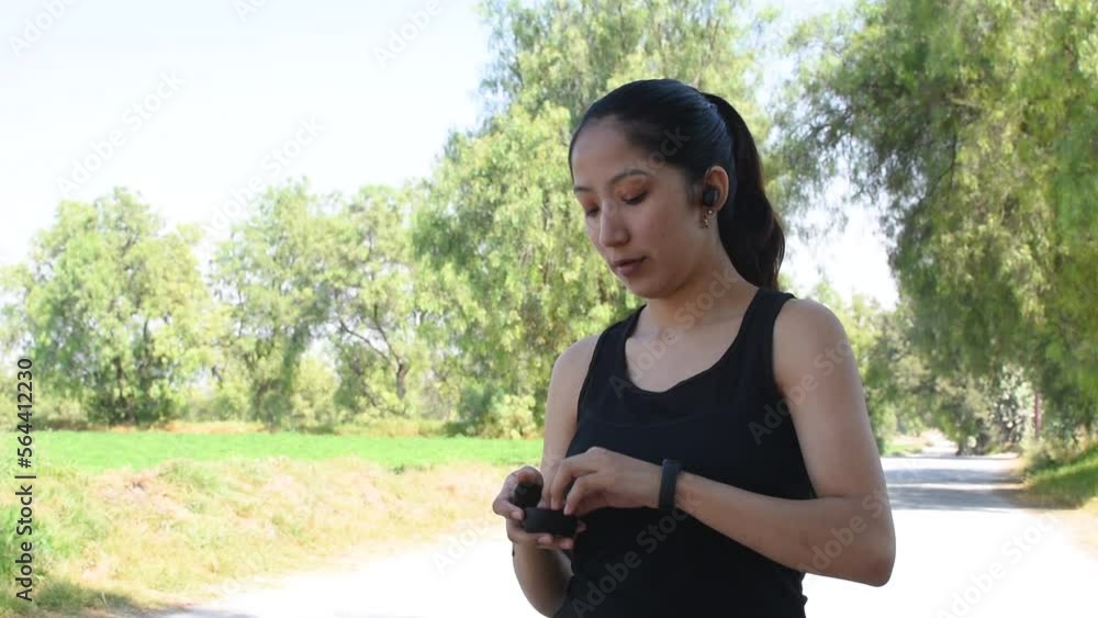 Joven mujer caucasica haciendo ejercicio y colocandose sus audifonos inalambricos antes de salir a correr en la naturaleza video en HD Joven mujer caucasica haciendo ejercicio y colocandose sus audifonos inalambricos antes de salir a correr en la naturaleza video en HD