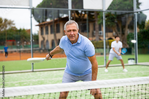 Emotional mature man playing paddle tennis couple match at outdoors court. Health and active lifestyle concept