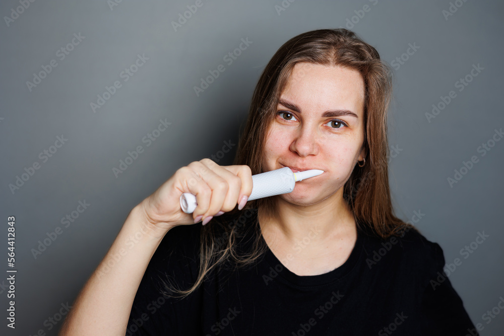 Obraz premium Portrait of a smiling young woman without makeup in a black t-shirt brushing her teeth, mature woman, natural beauty concept. Morning brush for teeth, dental ultrasonic brush.