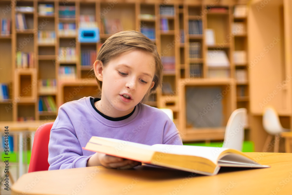 boy reading a book, doing homework while sitting at a table in a classroom or library boy reading a book, doing homework while sitting at a table in a classroom or library