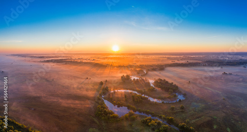 The channel and bends of the river, on a marshy meadow. Orange dry grass, scorched by the summer heat, and morning fog. A wonderful landscape at dawn. Drone view.