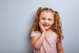 Emotional fun kid girl smiling with hand at face and looking happy with ponytail hairstyle on blue background. Closeup portrait