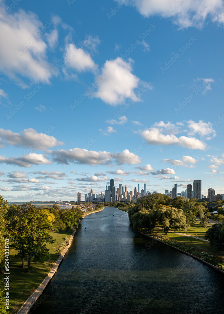 Naklejka premium Aerial view of the downtown Chicago city skyline from above the South Lagoon canal as rowing boats and a standup paddleboard make their way through the calm water on a sunny blue sky day.