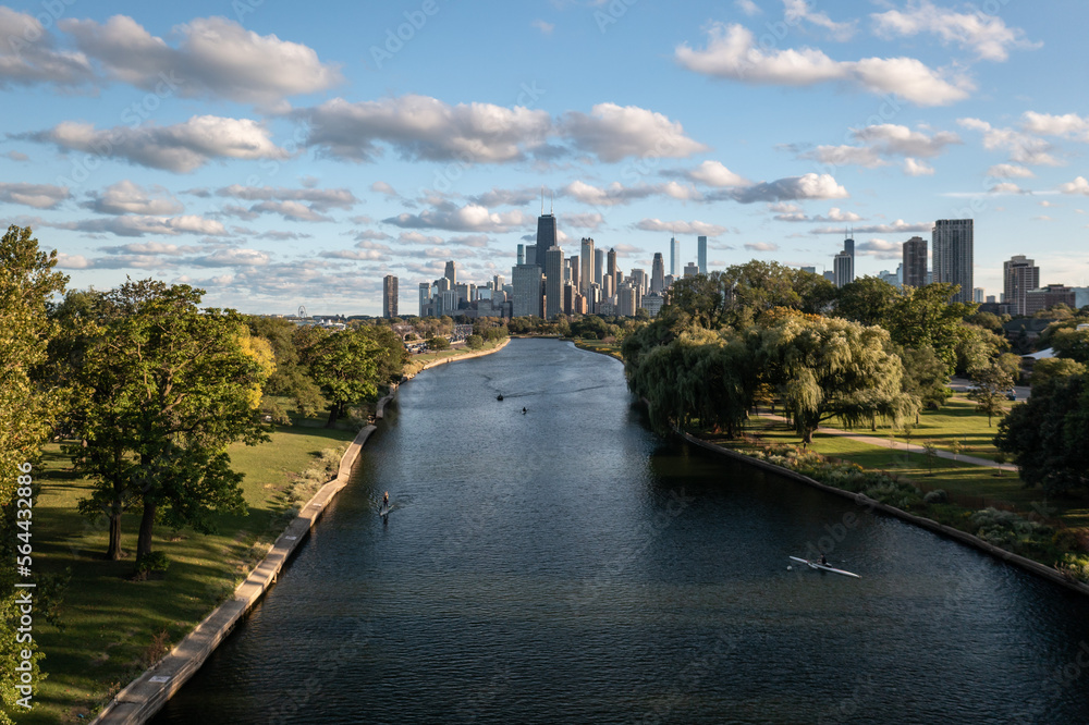 Aerial view of downtown Chicago skyline as a few people use the South Lagoon canal for standup paddle boarding, boating and rowing on a sunny day with blue sky and fluffy white cumulus clouds above.