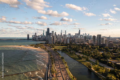 Downtown Chicago city skyline aerial centered over traffic along Lake Shore Drive between South Lagoon and Lake Michigan on a sunny day with fluffy white clouds in a blue sky above.