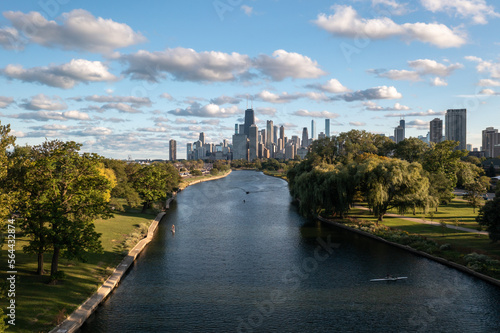 Aerial view of downtown Chicago skyline as a few people use the South Lagoon canal for standup paddle boarding, boating and rowing on a sunny day with blue sky and fluffy white cumulus clouds above. © Joseph Kirsch