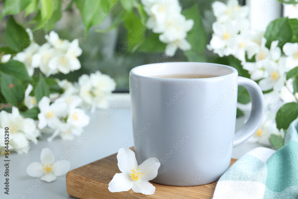 Cup of tea and fresh jasmine flowers on light grey table