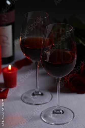 Glasses of red wine, rose flowers and burning candle on white table. Romantic atmosphere