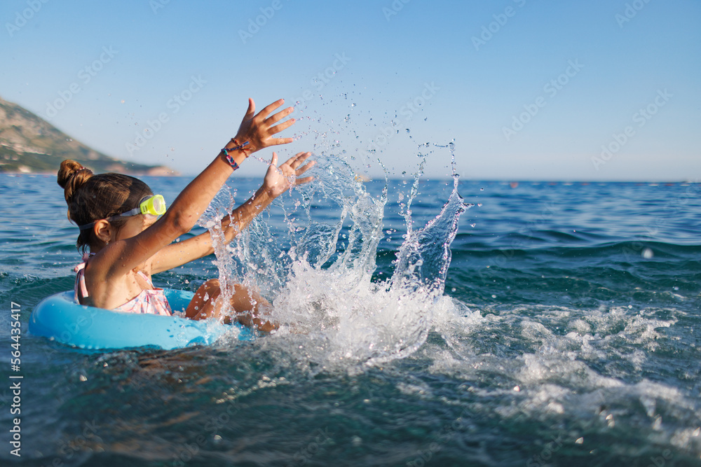 Cheerful girl sits in an inflatable circle and splashes with water in the sea