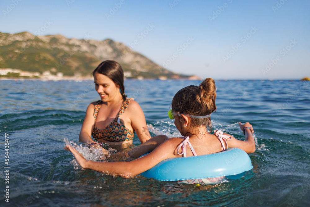 Obraz premium Two sisters in bathing suits play with an inflatable ring in the sea