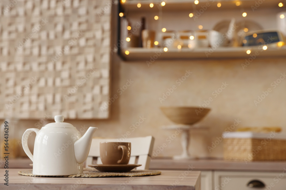White teapot with cup on wooden table in kitchen, space for text White teapot with cup on wooden table in kitchen, space for text