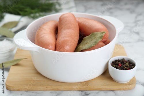 Bowl of delicious sausages, dill, bay leaf, pepper and salt on white marble table photo