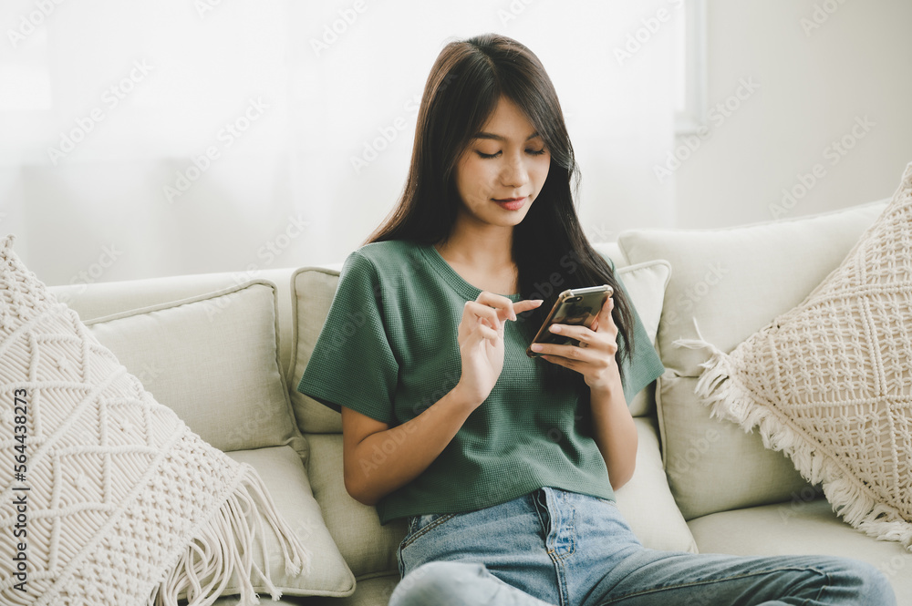 Happy young asian woman relaxing at home she is sitting on sofa and using mobile smartphone Happy young asian woman relaxing at home she is sitting on sofa and using mobile smartphone
