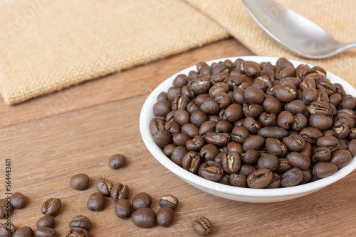 medium roasted peaberry coffee beans in a ceramic dish on wooden table, close up.