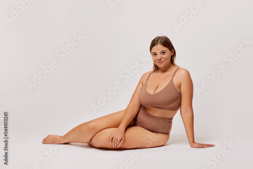 Plus size self enjoyed woman wearing lingerie sitting on a floor isolated over white background. Body Positive concept