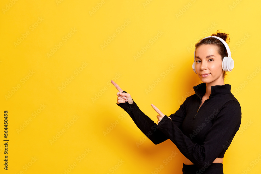 Young woman showing banner, pointing fingers left and smiling at camera, standing next to yellow background Young woman showing banner, pointing fingers left and smiling at camera, standing next to yellow background